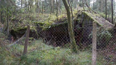 Der Maschendrahtzaun an einem ehemaligen Bunker ist teilweise niedergedrückt.