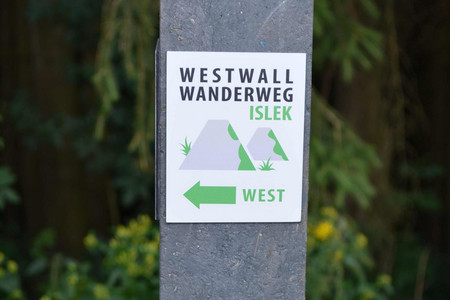 Wegweiser des Westwall-Wanderwegs Islek mit der Darstellung zweier bewachsener Höcker..