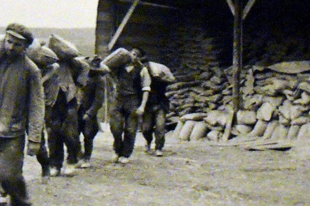 Männer der Organisation Todt tragen beim Westwallbau auf den Schultern Säcke von einem Schuppen fort.