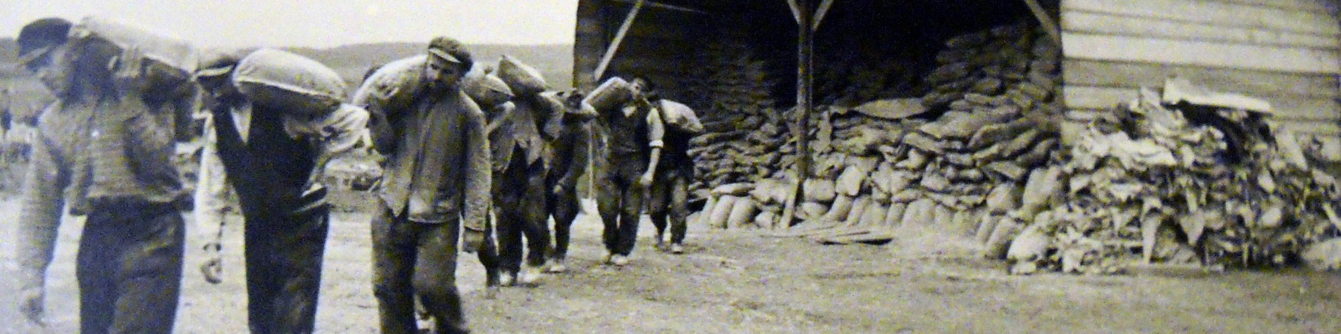 Männer der Organisation Todt tragen beim Westwallbau auf den Schultern Säcke von einem Schuppen fort.
