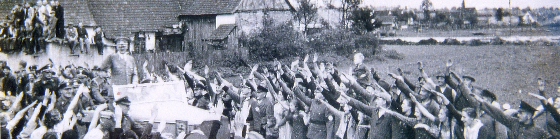 Hitler fährt in einem offenen Wagen 1939 durch Steinfeld. An beiden Seiten der Straße stehen Menschen.